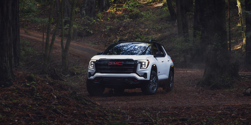Front view of a white GMC Terrain driving through a dark, wooded forest.