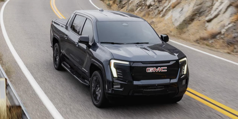 view of a dark gray GMC Sierra EV truck driving along a winding mountain highway.