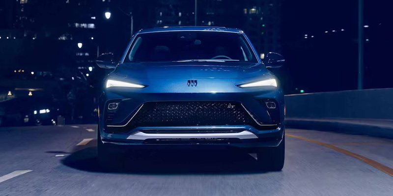 Front head-on view of a blue Buick Envista Sport Touring driving along a city street at night.