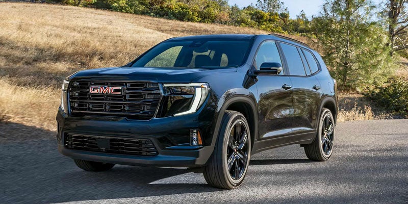 Dark blue 2026 GMC Acadia driving on a road.