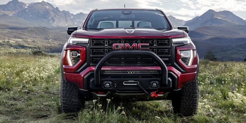 Front head-on view of a dark red GMC Canyon AT4X pickup truck parked in a mountain meadow.